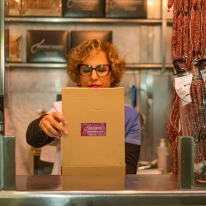 Empleado de charcutería empaquetando una caja gourmet con embutidos para envío o regalo.