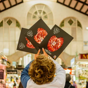 Comerciante en Valencia levantando tres estuches de jamón Oro Blanco en forma de corazón dentro del Mercado Central