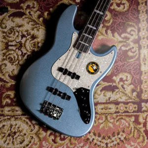 Bajo eléctrico azul metalizado con golpeador perlado, sobre alfombra vintage en estudio musical.
